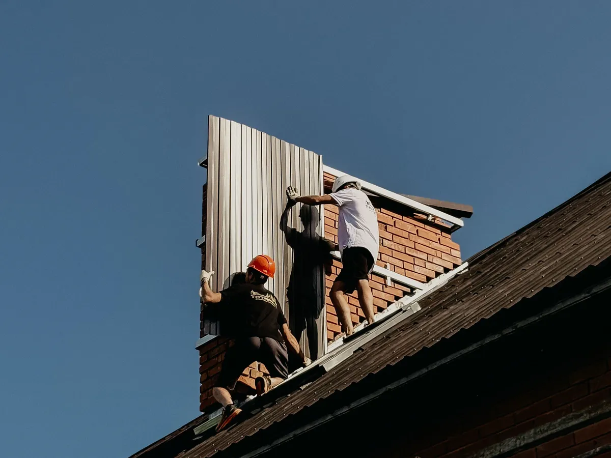 Two roofers installing metal panels on a gable