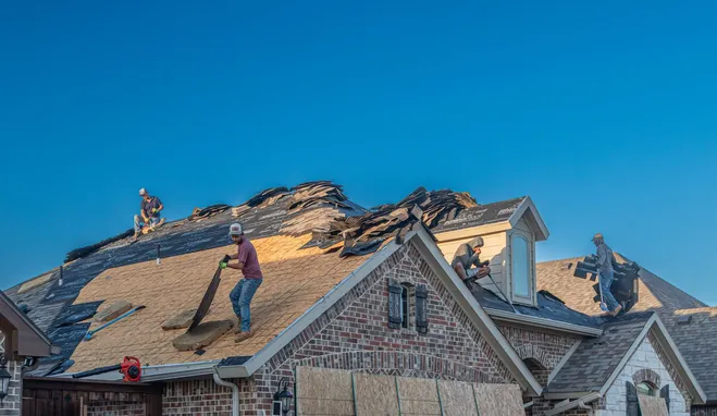 Roofing crew tearing off and replacing shingles on a brick home, work truck parked in the driveway