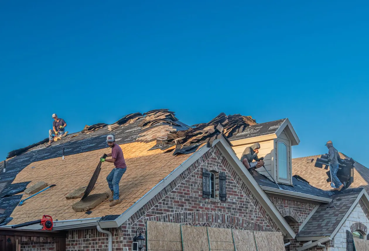 Roofing crew tearing off and replacing shingles on a brick home, work truck parked in the driveway