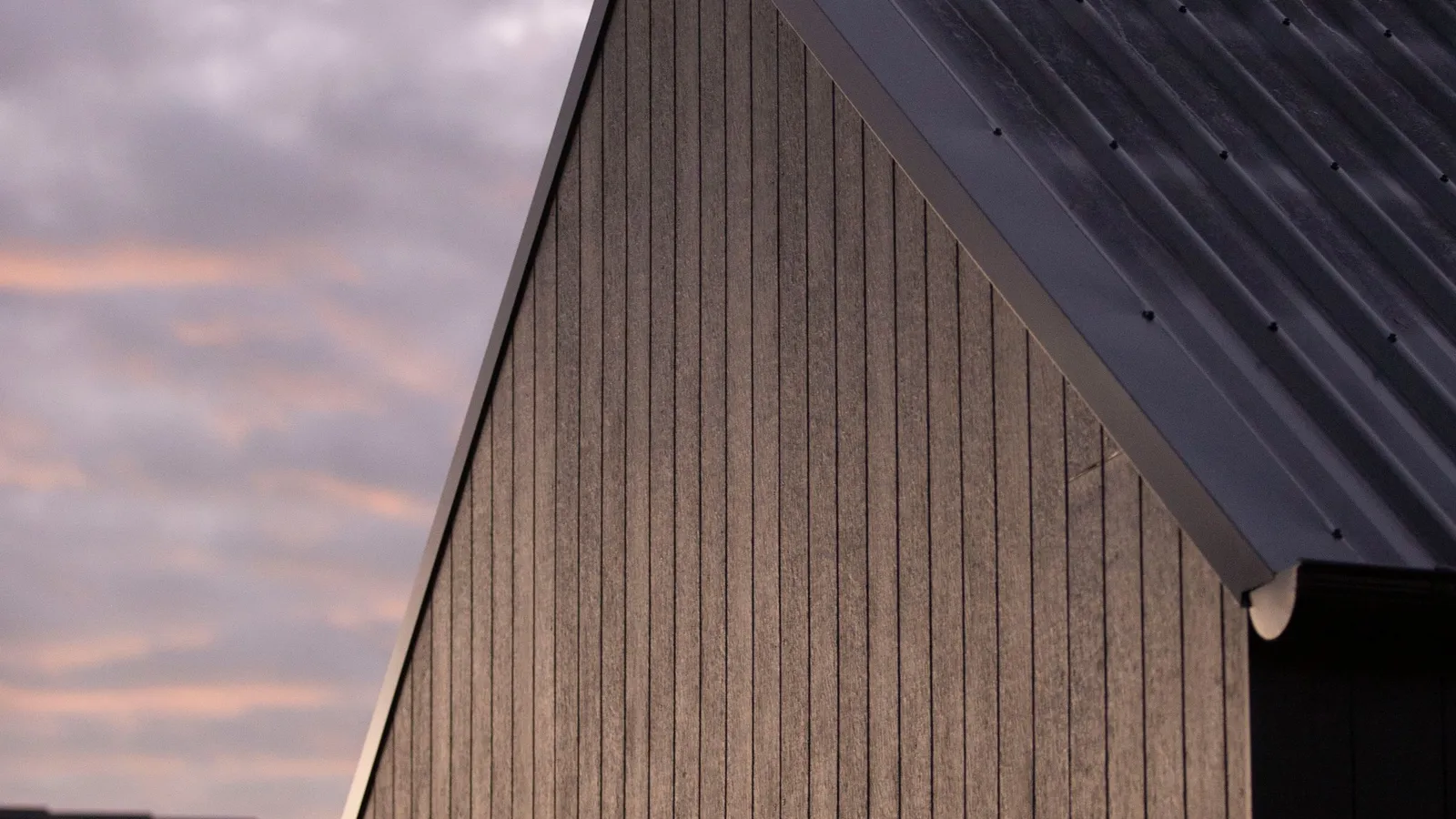 Dark standing-seam metal roof gable at dusk with warm sky