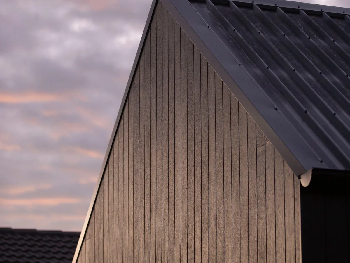 Dark standing-seam metal roof gable at dusk with warm sky