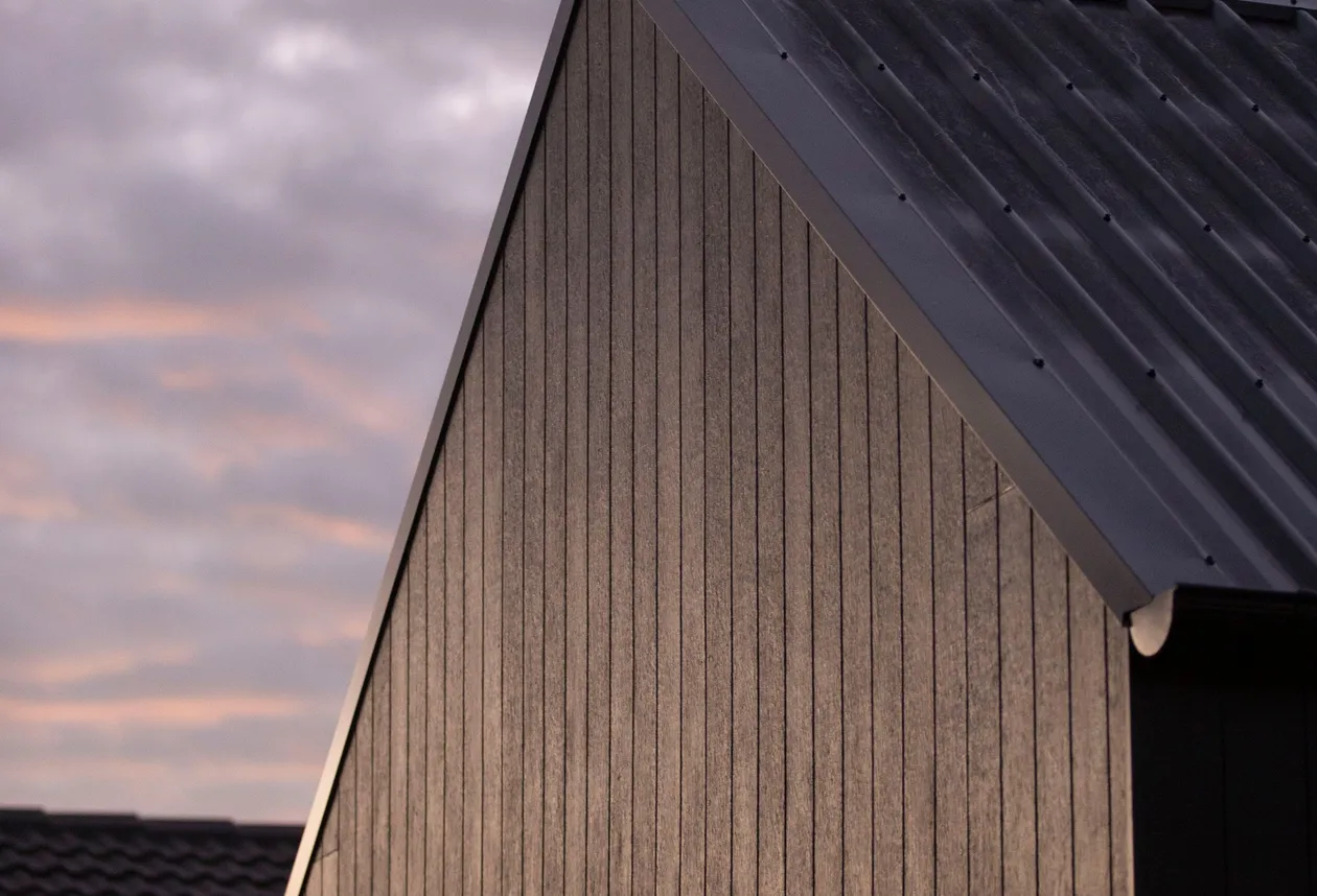 Dark standing-seam metal roof gable at dusk with warm sky