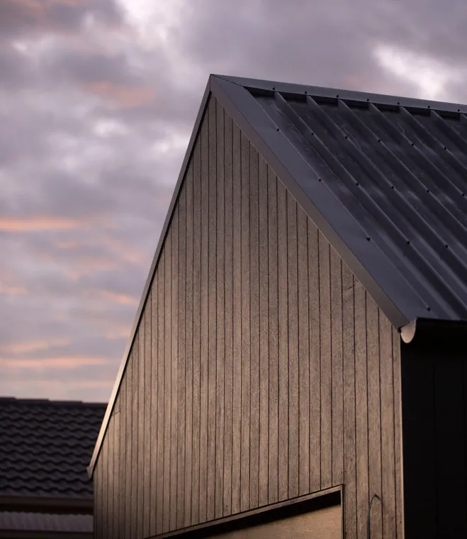Dark standing-seam metal roof gable at dusk with warm sky